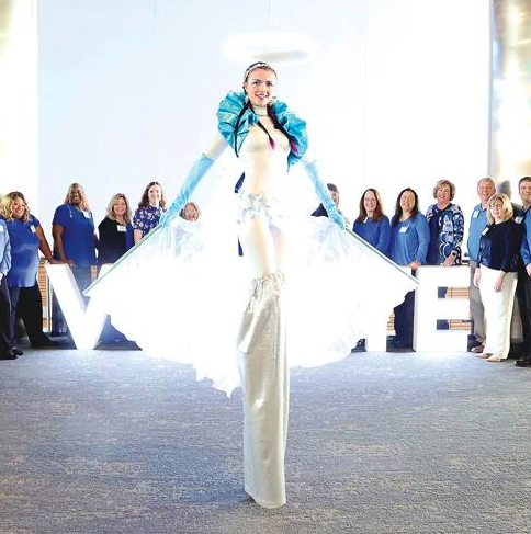 girl in fancy white and blue outfit, on stilts, standing in front of VOLUTE sign and VOA Oklahoma staff